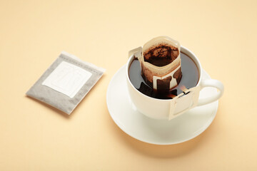 Drip coffee bag with ground coffee in cup on beige background