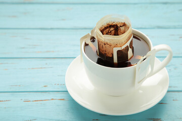Drip coffee bag with ground coffee in cup on blue wooden background