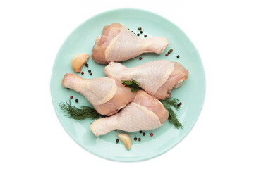Raw chicken drumsticks with spices on plate isolated on white background.