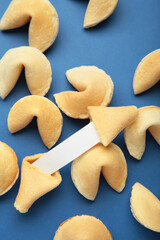Tasty fortune cookies and paper with prediction on blue background. Top view. Vertical photo