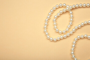 Elegant pearl necklace on beige background, top view. Space for text