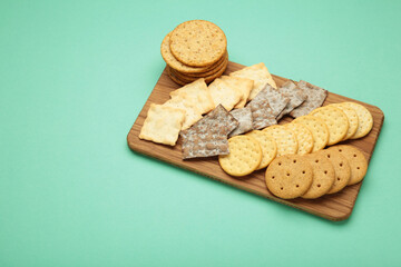 Different crackers on cutting board on mint background. Space for text