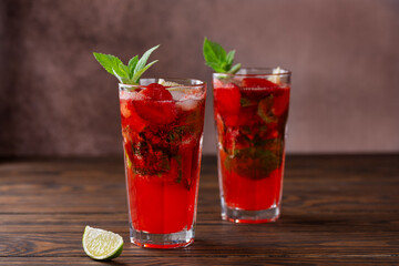 Cold strawberry Mojito cocktail with lime, ice and mint on a brown wooden table. Sugar free, nonalcoholic.