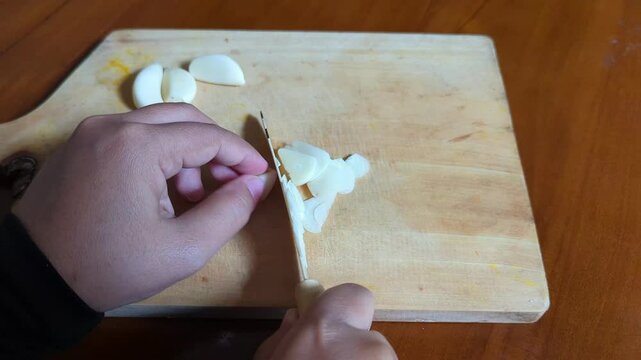 Close up a hand-chopped garlic on a wooden cutting board with a kitchen knife. Cooking preparation. Fast chopping, chef, cooking, carrots, cutting board, Organic food.