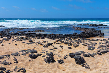 Tranquil beach scene showcasing rugged rocks along the shoreline. Beach is mostly empty, with only a few rocks scattered around. Scene is calm and peaceful, with the waves crashing in the background