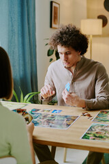 Vertical over shoulder shot of young biracial man and his girlfriend spending spare time at home playing board game