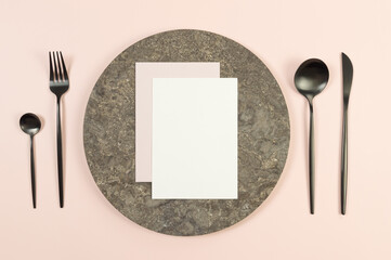 Top view of brown marble plate, black cutlery on pink background. White and pink cards. Food presentation, stone tray. Table setting, copy space, flat lay.
