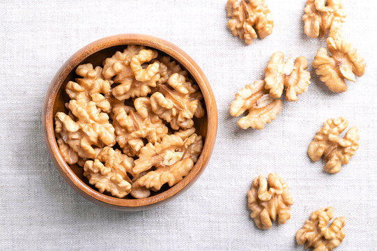 Walnut kernel halves in a wooden bowl on linen fabric. Shelled and dried halves of walnut kernels, ripe seeds of common walnut tree Juglans regia, used as snack or for baking. Close-up from above.