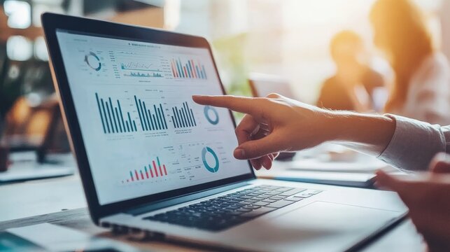 Hand pointing closely at detailed data and analytical graphs displayed on a laptop screen during a business meeting, emphasizing critical information analysis.