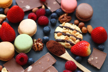 Macarons, chocolate, cookies, berries and various nuts on dark blue background. Selective focus.