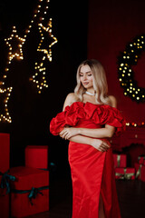 Blonde woman in red dress posing in front of Christmas tree. High quality photo