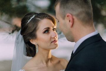 A bride and groom are standing close to each other, with the bride wearing a veil and the groom wearing a suit