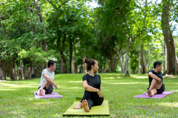 Three people are doing yoga on a green mat in a park