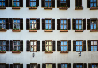 Old building facade with pattern of open old windows with wooden jalousie and flowers in Innsbruck. Historical architecture or medieval exterior with opened timbered blinds or louver. Austria