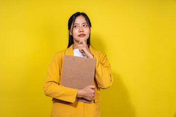 Obraz premium A woman in a yellow jacket is holding a clipboard and looking to her right