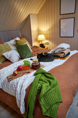 A gray cat lies on the bed next to a tray of coffee and flowers on a white plaid blanket 