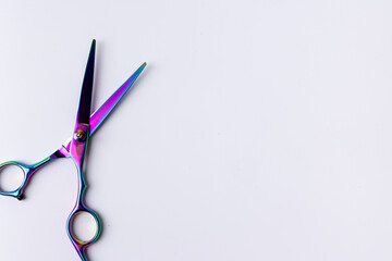 Close-up view of open scissors on a white surface, seen from above. The scissors are aligned to the left