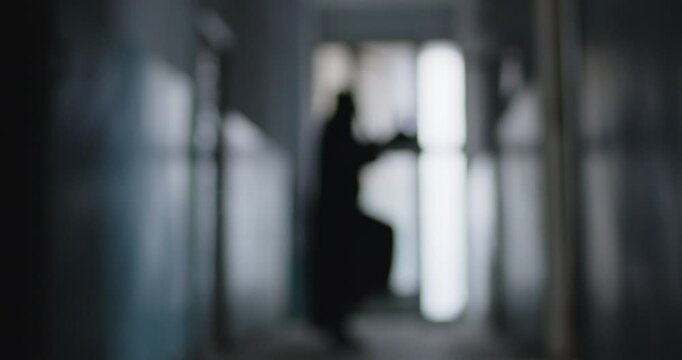 Blurred shot of a grim reaper dancing with a scythe in the dark corridor. This creepy and fun scene blends fear and horror. Halloween night. Funny dance of a figure in a death costume.