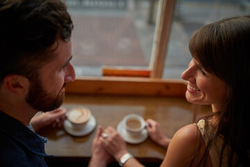 Coffee shop, happy and couple holding hands with drink, caffeine beverage and cappuccino in cafe. Dating, love and man and woman relax in restaurant for bonding, relationship and romance on weekend