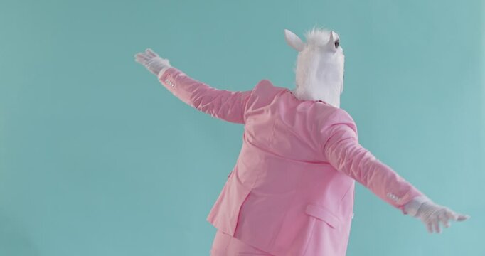 Funny dancing man wearing cute horse head mask, formal beautiful pink pastel color stylish suit, gloves, charming animal dance representation for party show, strange dancer moving with open hands