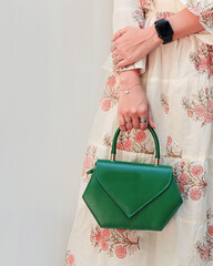 Leather purse handbag on female hand. Women's outfit and lifestyle accessories concept. Green purse handbag for female outfit. Hand holding a purse.