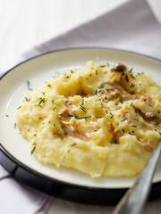 A plate of creamy mashed potatoes topped with a rich, savory gravy and garnished with fresh herbs. The dish is served on a white plate, with a spoon placed on the side, ready to be enjoyed