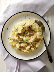 A plate of creamy mashed potatoes topped with a rich, savory gravy and garnished with fresh herbs. The dish is served on a white plate, with a spoon placed on the side, ready to be enjoyed