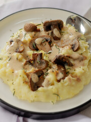 A plate of creamy mashed potatoes topped with a rich mushroom gravy and garnished with fresh rosemary. The dish is elegantly presented on a white plate, highlighting the hearty, comforting meal.