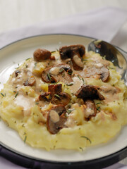A plate of creamy mashed potatoes topped with a rich mushroom gravy and garnished with fresh rosemary. The dish is elegantly presented on a white plate, highlighting the hearty, comforting meal.