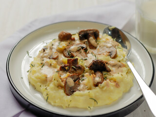 A plate of creamy mashed potatoes topped with a rich mushroom gravy and garnished with fresh rosemary. The dish is elegantly presented on a white plate, highlighting the hearty, comforting meal.