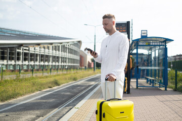 Tourist Caucasian business man traveler with bag and suitcase sit at public transport bus station waiting with mobile smart phone 