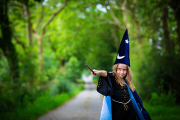 Caucasian blonde child girl in wizard blue costume with cape and hat, casting a spell with magic...