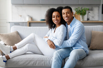 Home comfort. Loving black spouses relaxing, hugging while spending time together on weekend, couple cuddling in living room