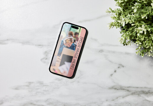 Black smartphone on a marble table with greenery. PSD mockup template