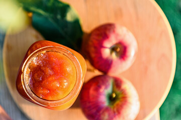 Glass jar of apple jam and fresh fruits on garden background.