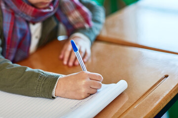Hand, student and books with writing, classroom and desk for learning, education and growth at...