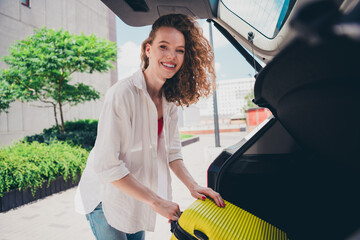 Photo of excited dreamy lady put valise car trunk tourist taxi airport wear white shirt walking outside modern urban city street