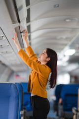 Woman Storing Luggage in Airplane Overhead Compartment: A young woman in a stylish yellow jacket...