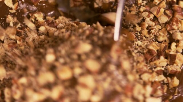 Mixing nuts with caramel, making salted caramel pecan candies, close up