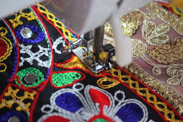 stitching machine closeup for sewing the floral design traditional navratri laces for chaniya choli. dress is getting ready by a tailor. stitching business for navratri festival in gujarat india. 