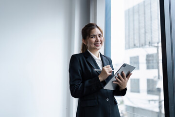 Confident Businesswoman in Modern Office Holding Tablet and Smiling by Window