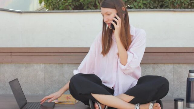 Woman working laptop and talking on smartphone on the street. 