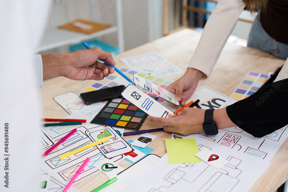 Wall mural creative team collaborating on ux ui design with colorful prototypes and wireframes on a wooden desk