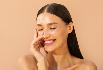 Portrait of young European brunette woman smiling with eyes closed, touching her face gently over...