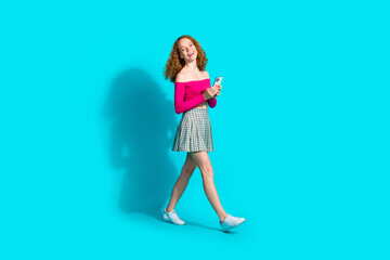 Full size photo of nice young girl walk hold phone wear top isolated on teal color background