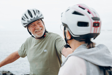 Senior couple riding bikes together in rocky beach enjoying outdoor. Active mature people talking and hugging each others. Bicycle lifestyle concept, having fun