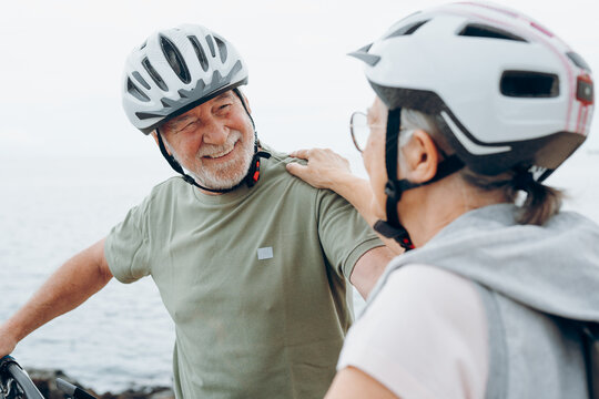 Senior couple riding bikes together in rocky beach enjoying outdoor. Active mature people talking and hugging each others. Bicycle lifestyle concept, having fun - Powered by Adobe