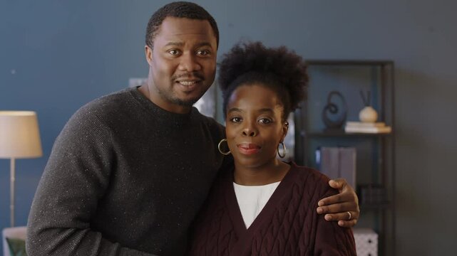 Medium slowmo portrait of Black man embracing his wife and both smiling at camera standing at modern psychologist office after family therapy session
