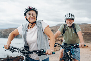 Senior couple riding bikes together in rocky beach enjoying outdoor. Active mature people talking holding mountain bikes. Bicycle lifestyle concept, having fun.