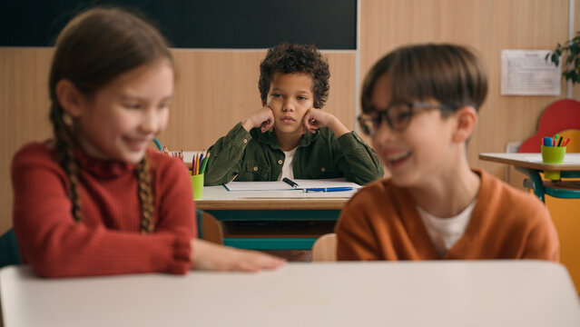 Two Caucasian children school lesson girl boy classmates laughing talk evil laugh mocking bully African American kid child schoolboy sad upset stressed lonely mock bullying kids class discrimination